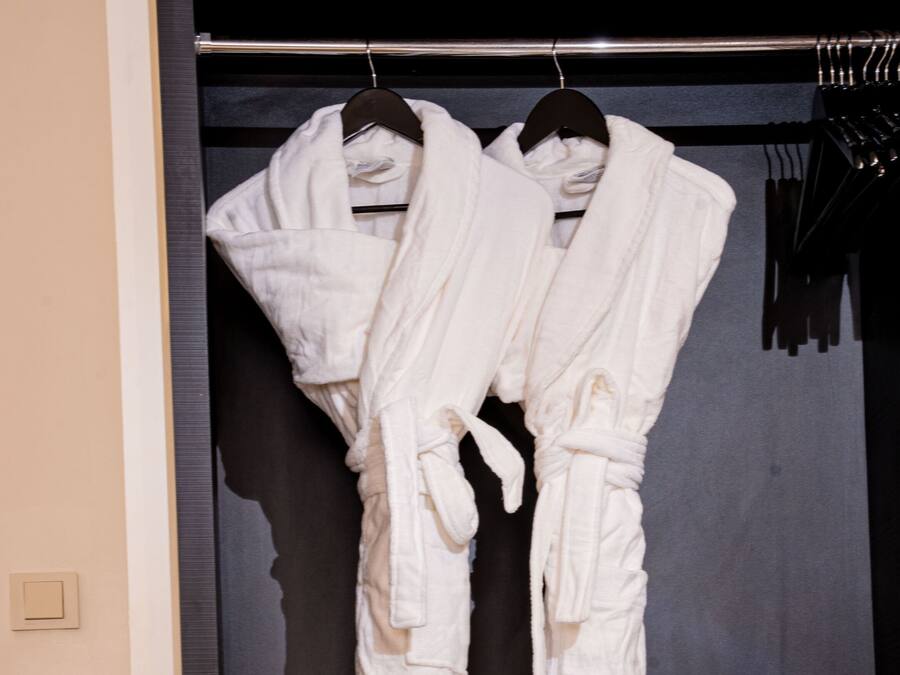 Una habitación de hotel con un armario que contiene albornoces y toallas blancos.