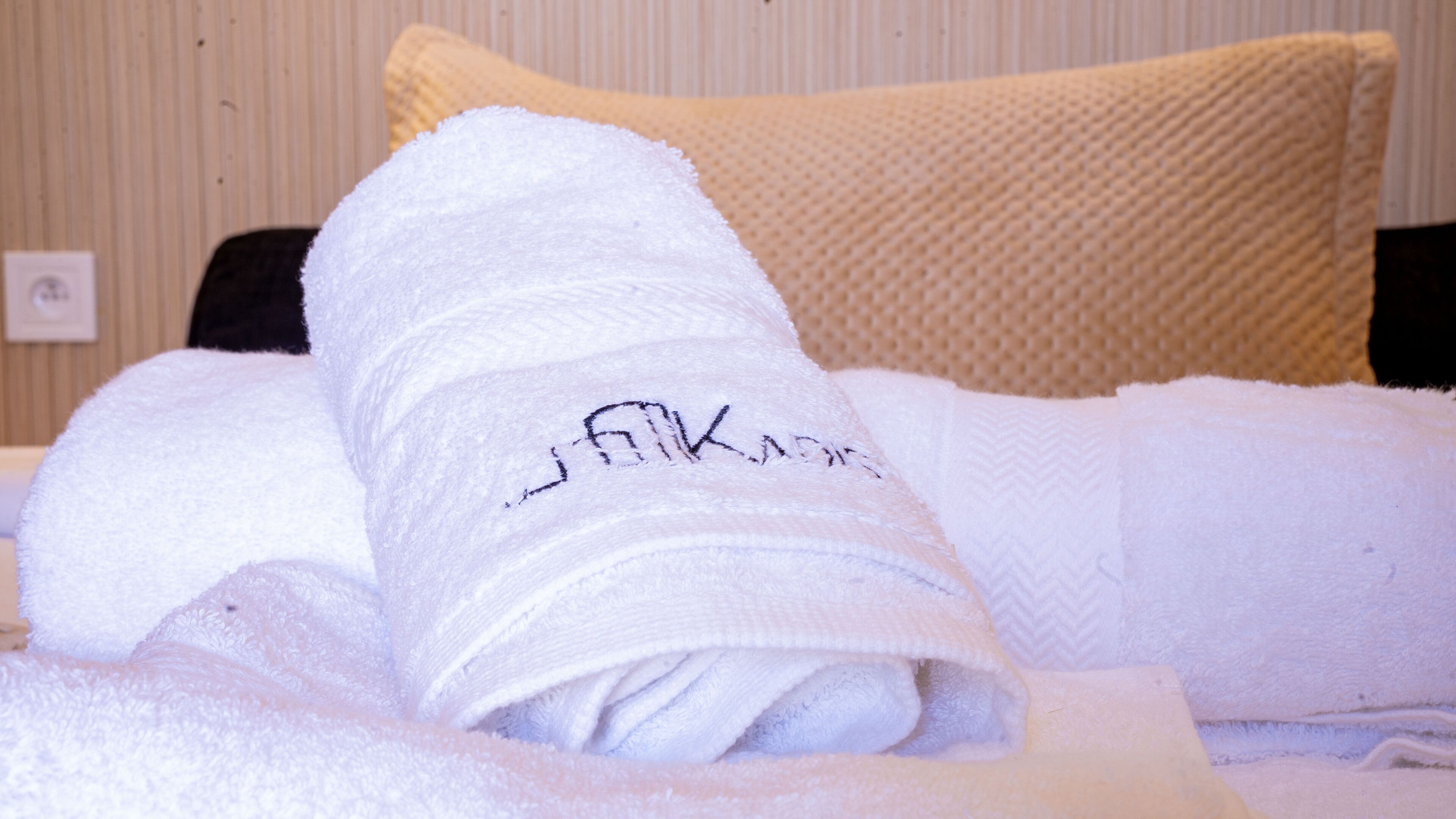 Una toalla blanca doblada con un logo sobre una cama con un almohadón amarillo con textura.