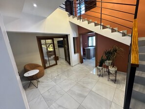 A spacious living area with a staircase, a dining table with chairs, and a kitchen area in the background.