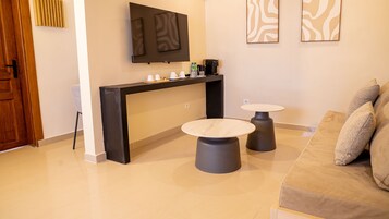 Una sala moderna con un mueble consola negro, dos mesas redondas, un sofá y un televisor de pantalla plana montado en la pared.