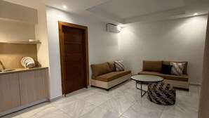 A modern living room with a sofa set, a coffee table, and a kitchen area with a counter and cabinets. - Kadiss Hotel (Dakar)