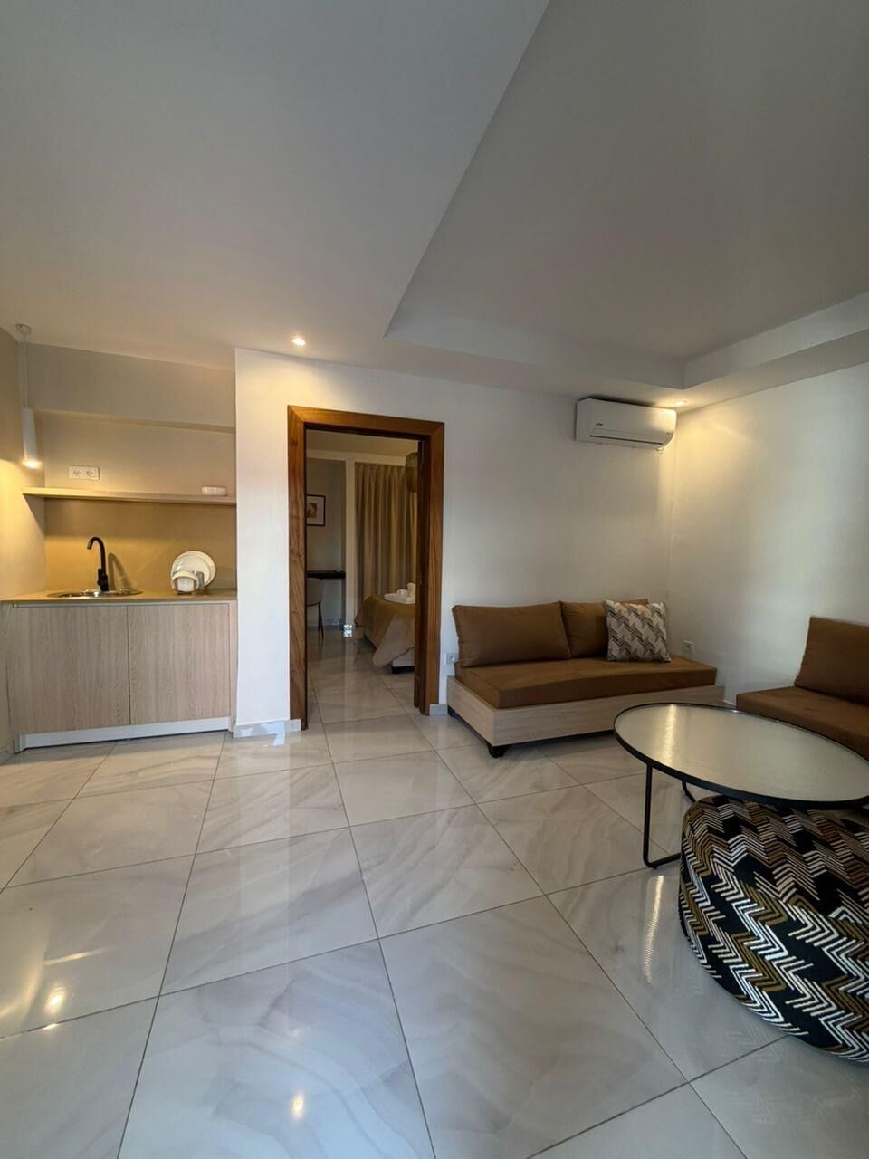 Una sala de estar moderna con un sofá, una mesa de centro y una cocina con un lavamanos y alacenas.