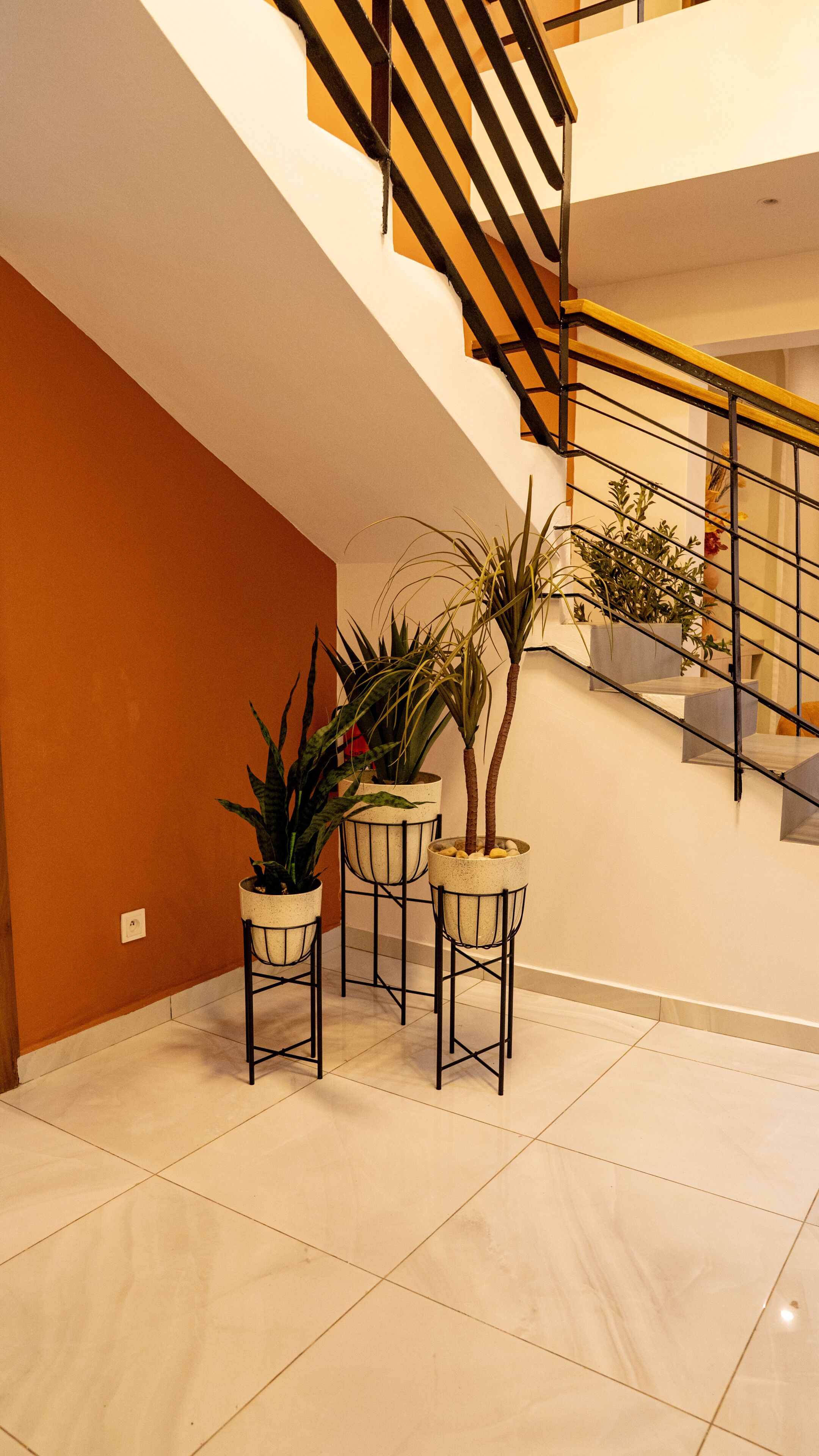 A staircase with a wooden handrail and metal balusters, leading to an upper floor. There are potted plants on the lower floor.