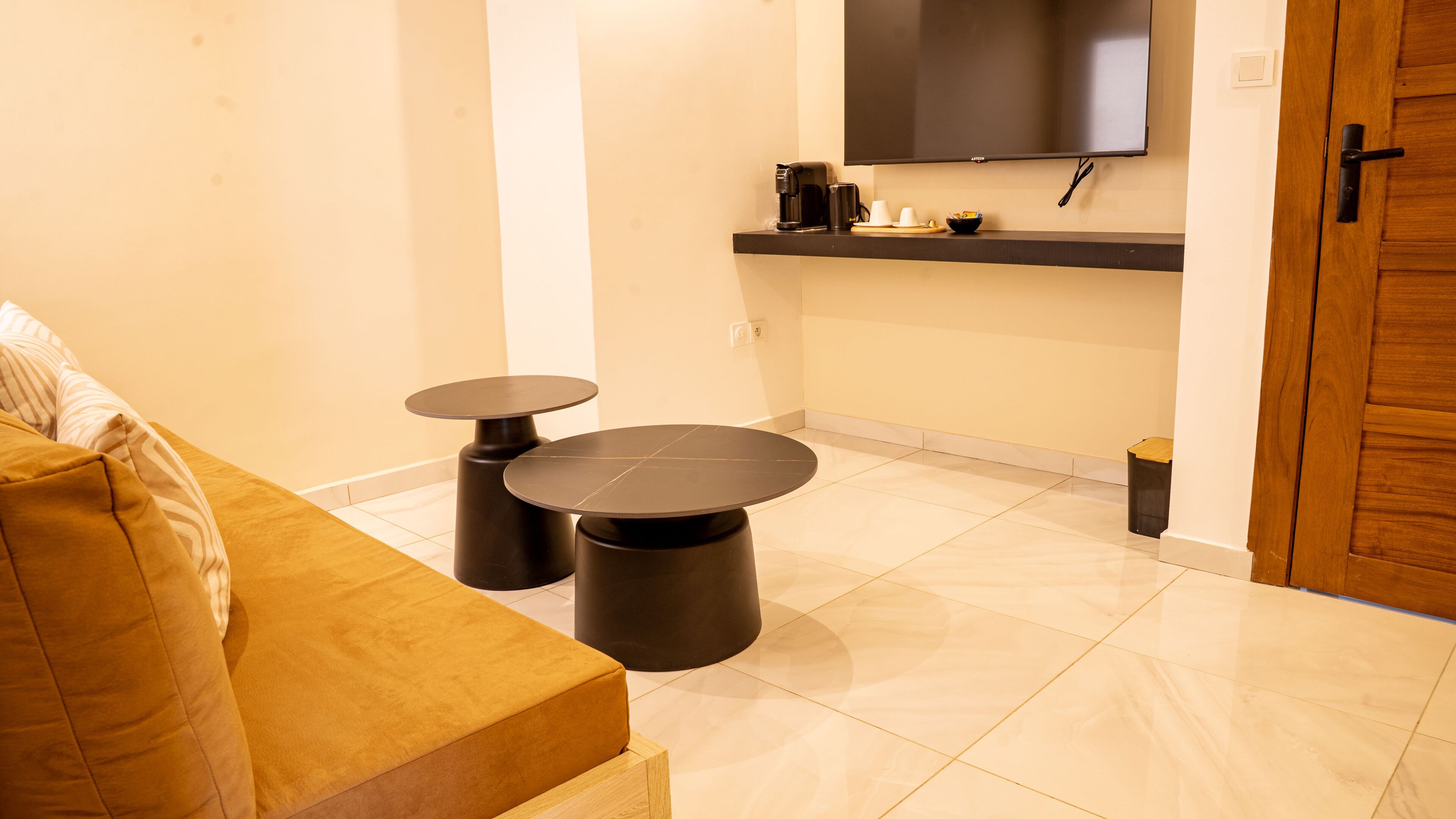 A modern living room with a sofa, two round tables, a coffee machine, and a TV mounted on the wall.