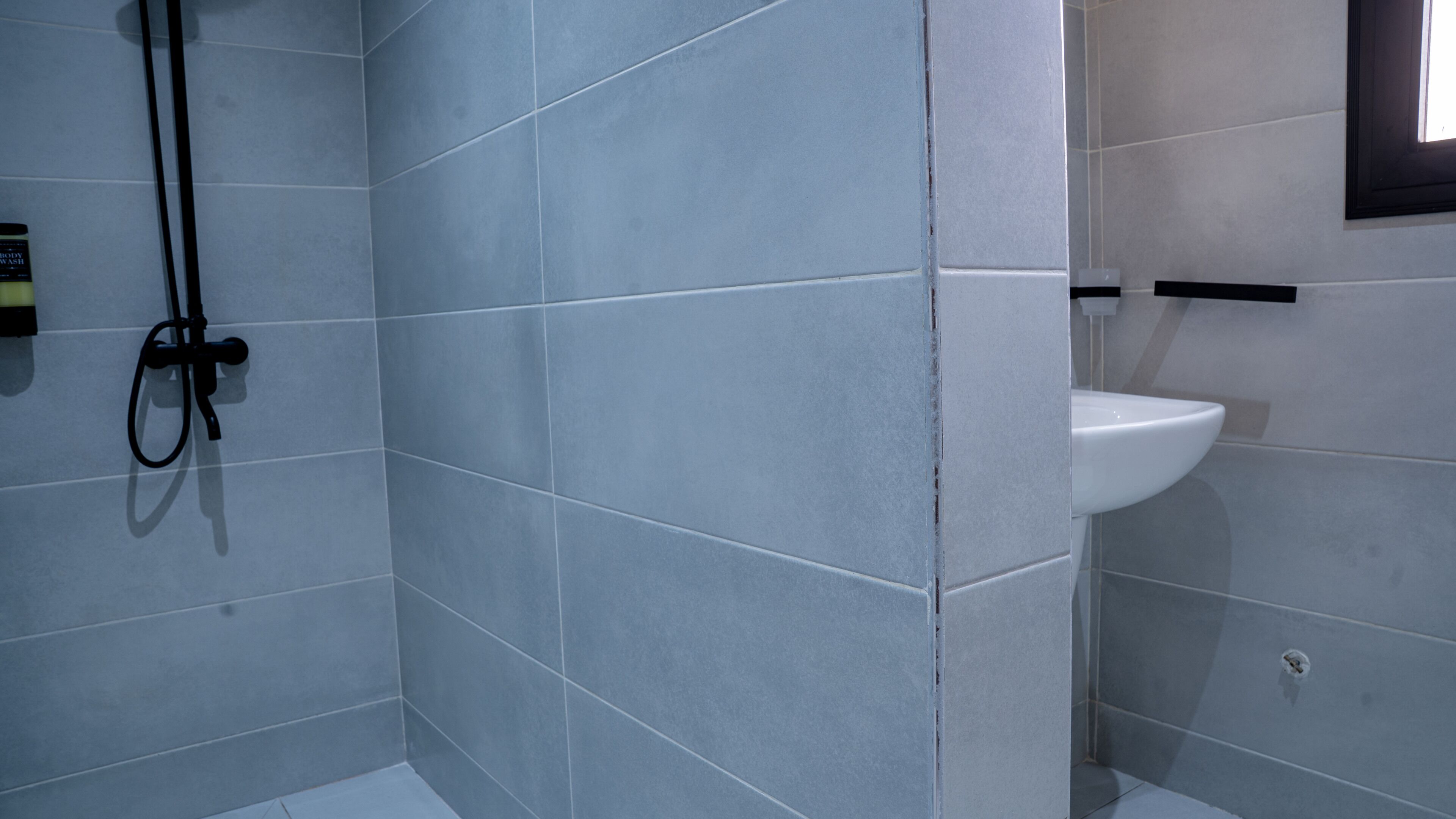 Casa de banho com paredes revestidas a azulejos cinzentos, uma sanita branca e um porta-toalhas preto.