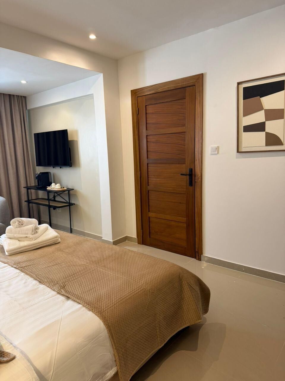 Habitación de hotel con cama, puerta de madera, televisor y una mesita con control remoto.