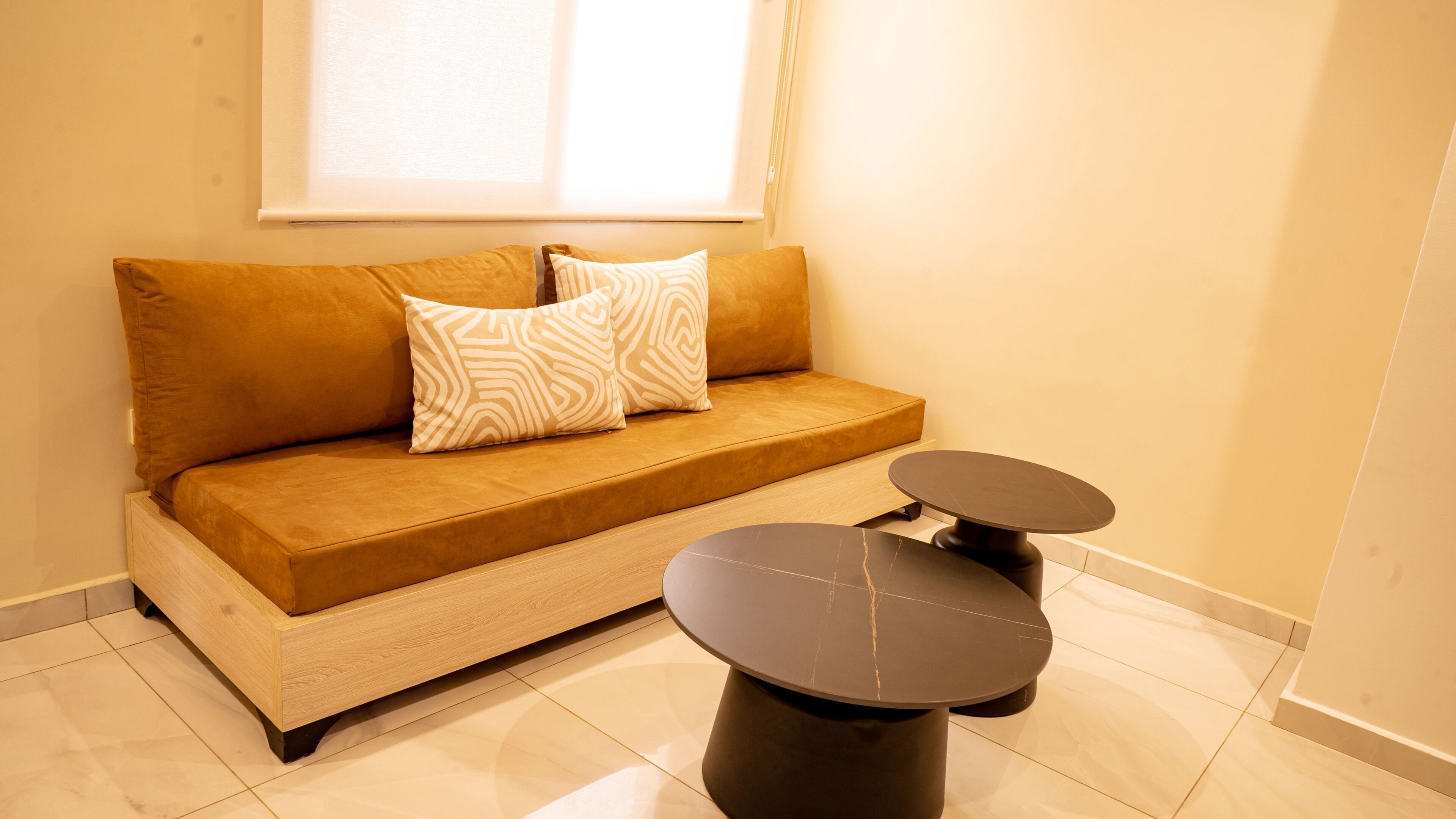 A modern living room with a sofa, two side tables, and a window with blinds.