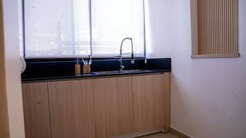 Eine Küche mit schwarzer Arbeitsplatte, Holzschränken, einer Edelstahl-Spüle und einem Fenster mit Jalousien.