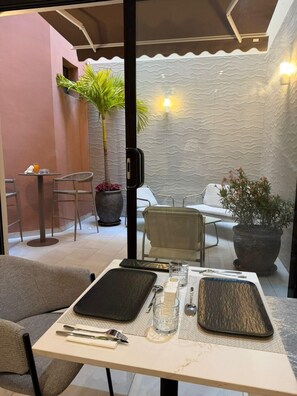 A dining area with a table set for two, a potted plant, and a seating area with chairs and a sofa.