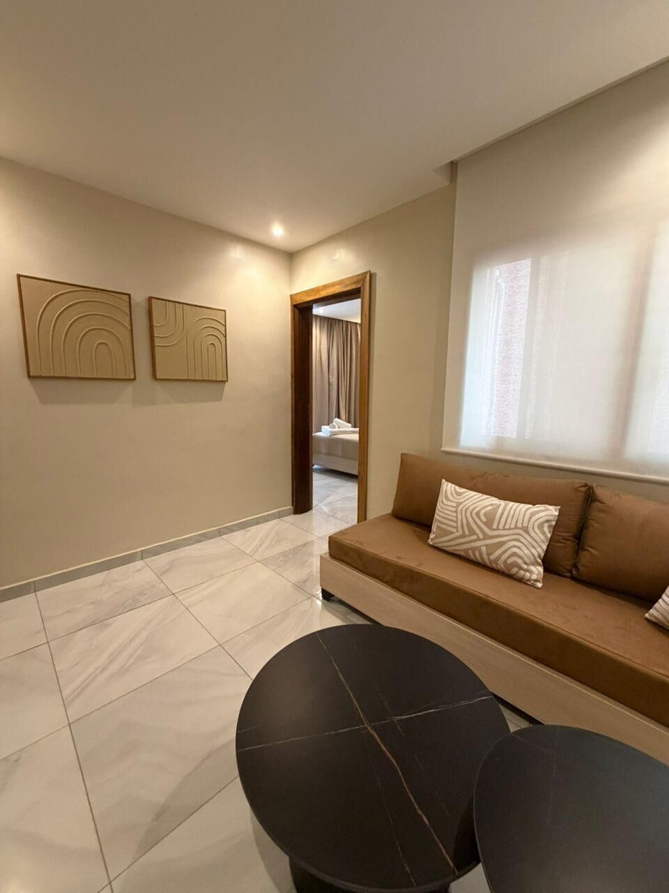 Un espace de vie moderne comprenant un canapé, deux tables noires et un couloir menant à une chambre.