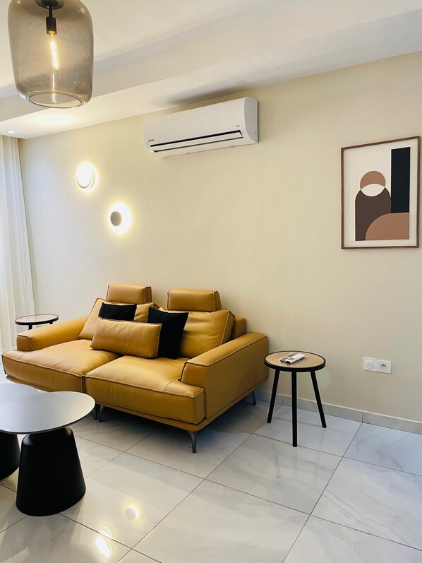 A modern living room with a sofa, a round table, and an air conditioning unit. - Kadiss Hotel (Dakar)