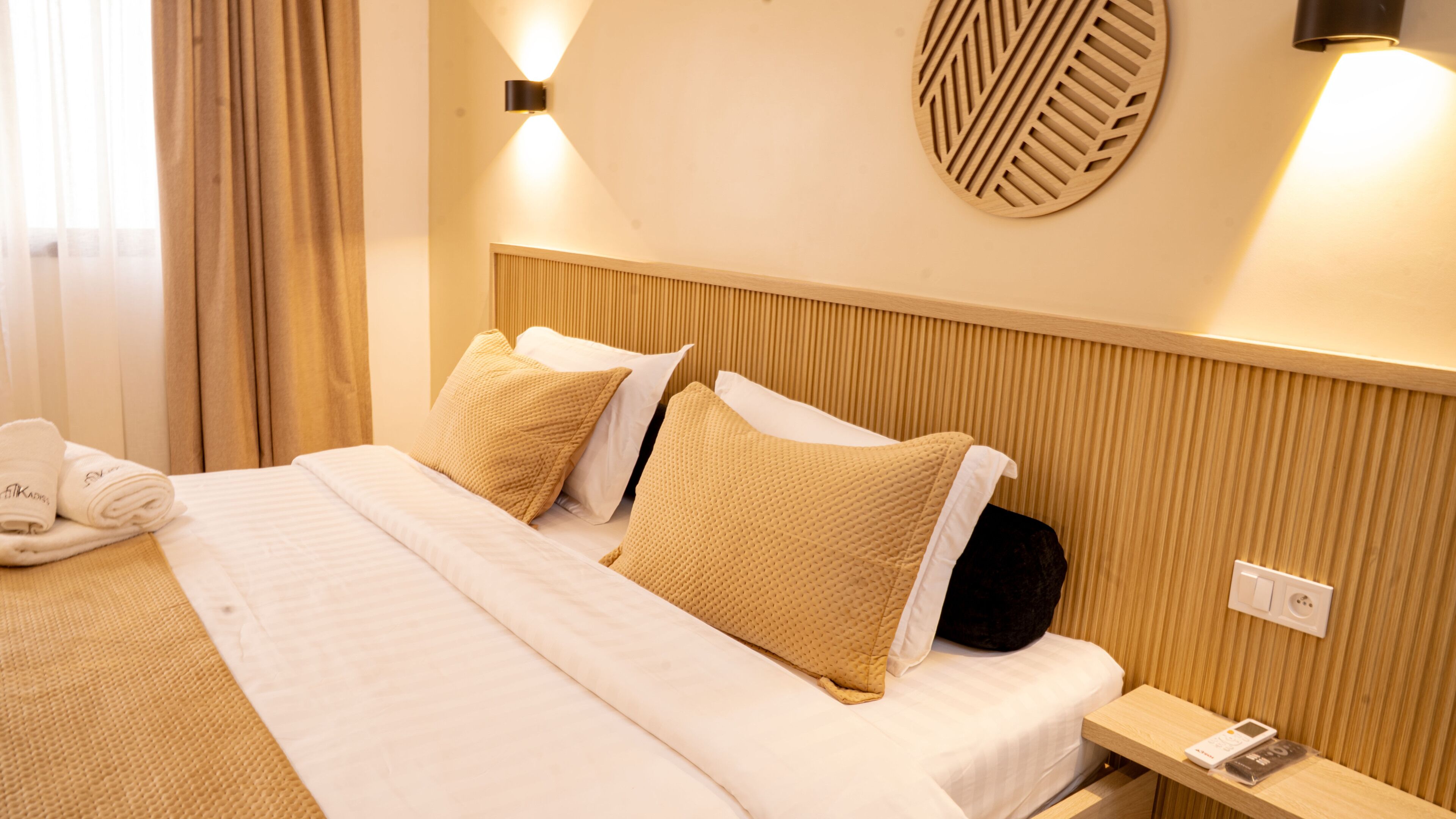 A hotel room with a bed, pillows, a bedside table with a phone, and a wall-mounted light fixture.