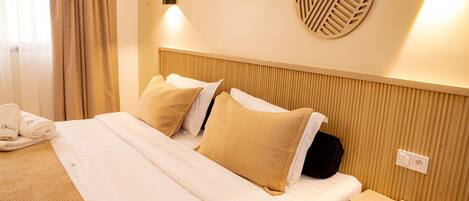 A hotel room with a bed, pillows, a bedside table with a phone, and a wall-mounted light fixture.