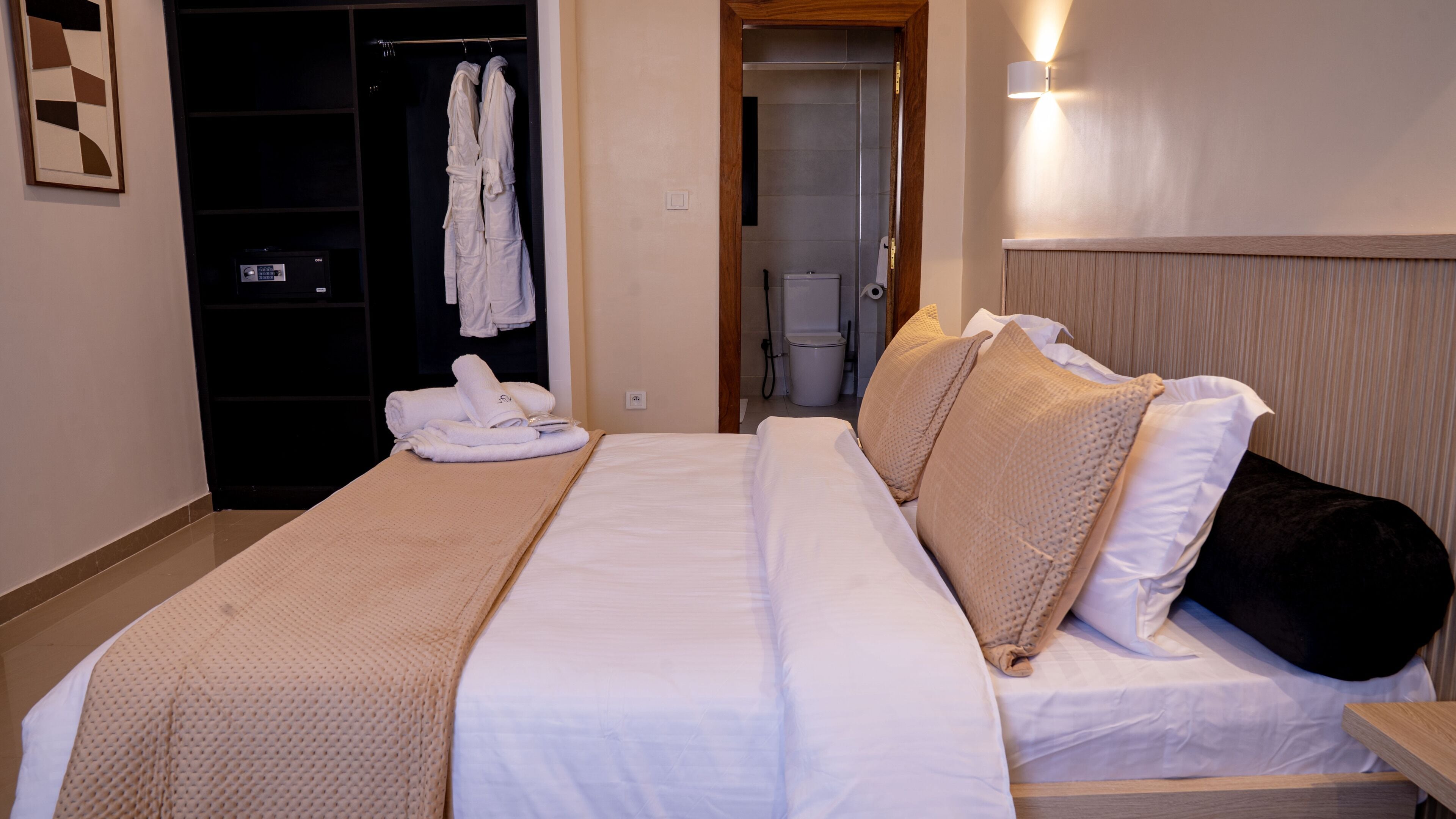 Une chambre d’hôtel avec un lit, une tête de lit en bois, une salle de bain visible à travers une porte ouverte et un porte-serviettes avec des serviettes.
