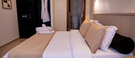 Une chambre d’hôtel avec un lit, une tête de lit en bois, une salle de bain visible à travers une porte ouverte et un porte-serviettes avec des serviettes.
