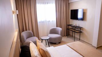 Habitación de hotel con cama, dos sillones, una mesita, televisor y cortinas.