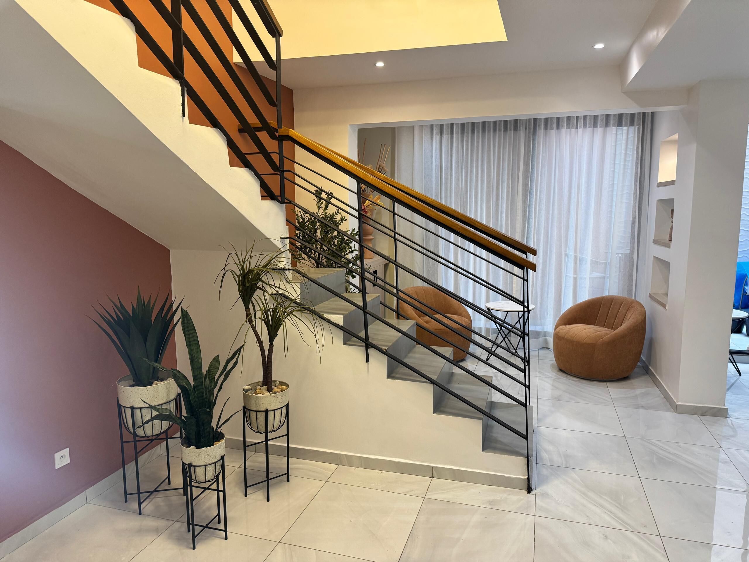 A modern staircase with a wooden handrail, a living area with a sofa and a coffee table, and potted plants.