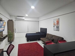 Ein kleines Zimmer mit Bett, Sofa, Schreibtisch und Fernseher.