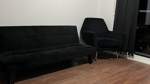 Huoneessa on musta sohva, musta tuoli ja puulattia.