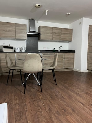 A modern kitchen with wooden cabinets, a gas stove, and a dining area with two chairs. - Bespoke 2 Bed Deansgate & Mediacity | Free parking (Salford)