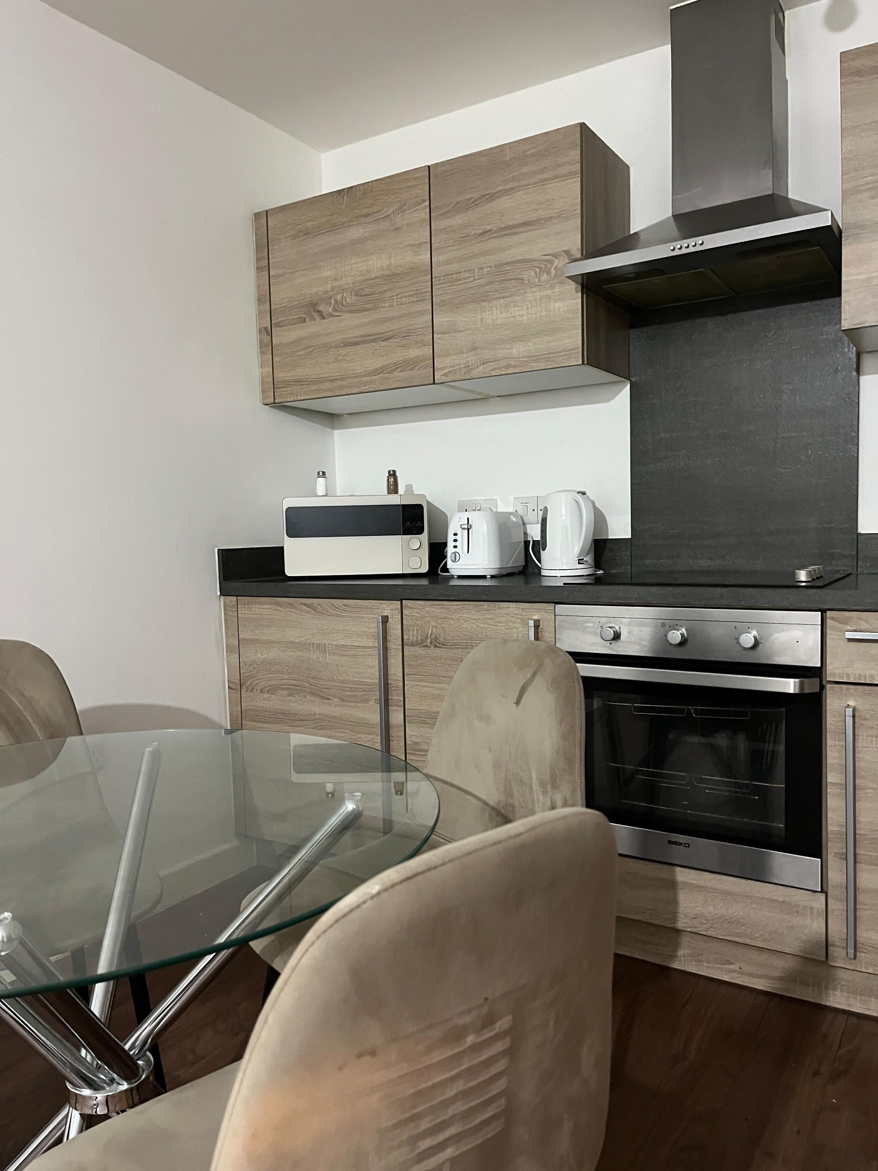 Une cuisine moderne avec des meubles en bois, une table à manger en verre, un four encastré et un four à micro-ondes.