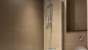 Moderni kylpyhuone, jossa on lasiseinällä varustettu suihku, valkoinen kylpyamme ja wc.