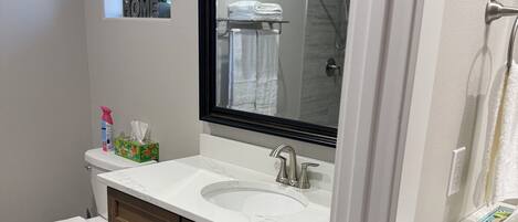 A bathroom with a toilet, a sink with a large mirror, wooden cabinets, and a window with a view of the outside.