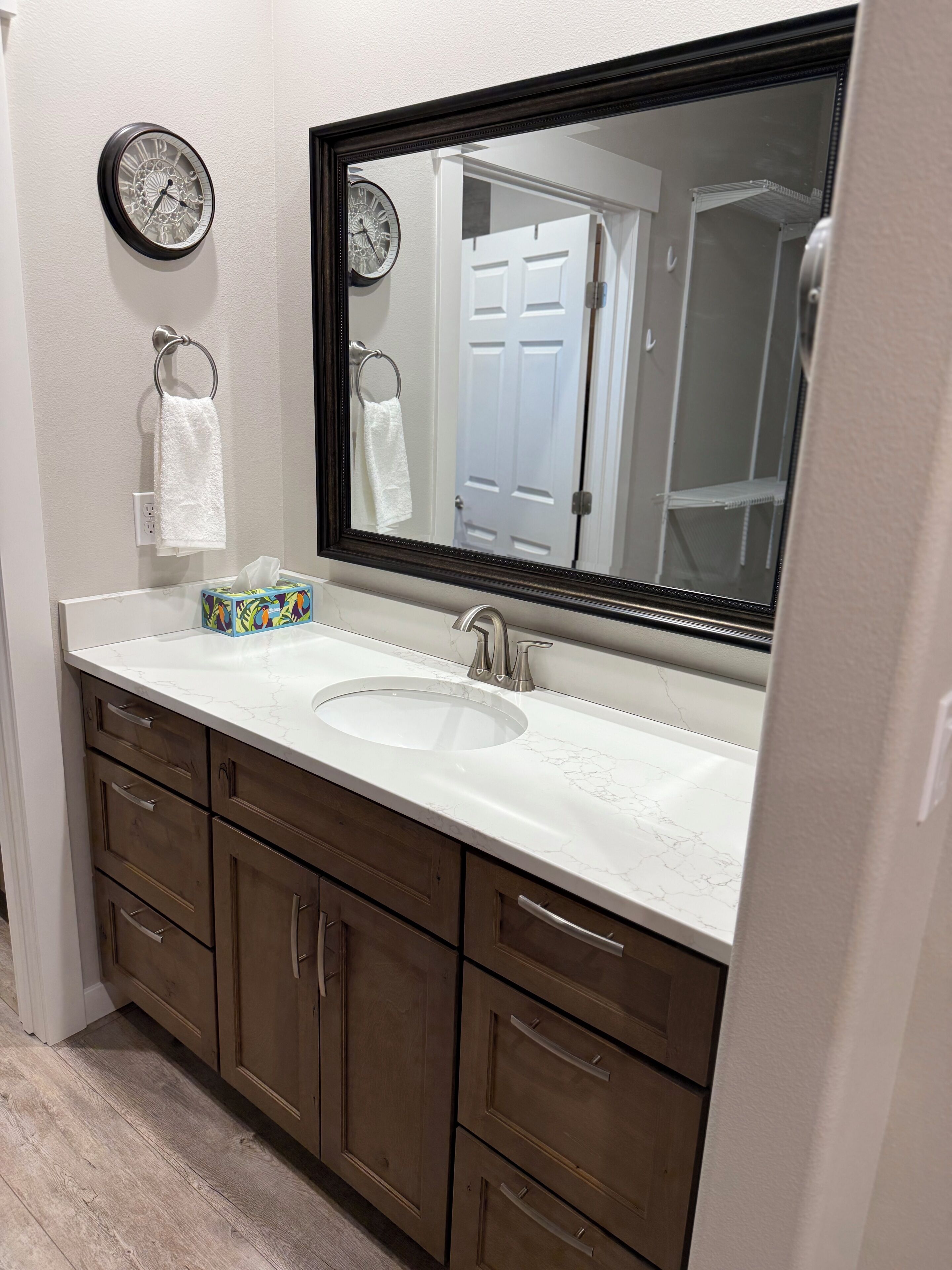 Une salle de bain avec un grand miroir, un lavabo, des meubles en bois et une horloge au mur.