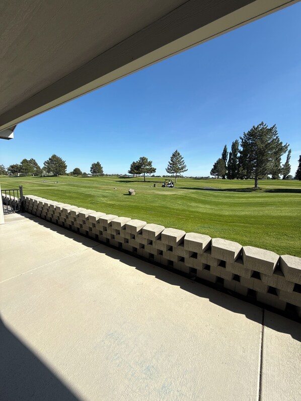 A view from a covered porch to a golf course with a clear sky.