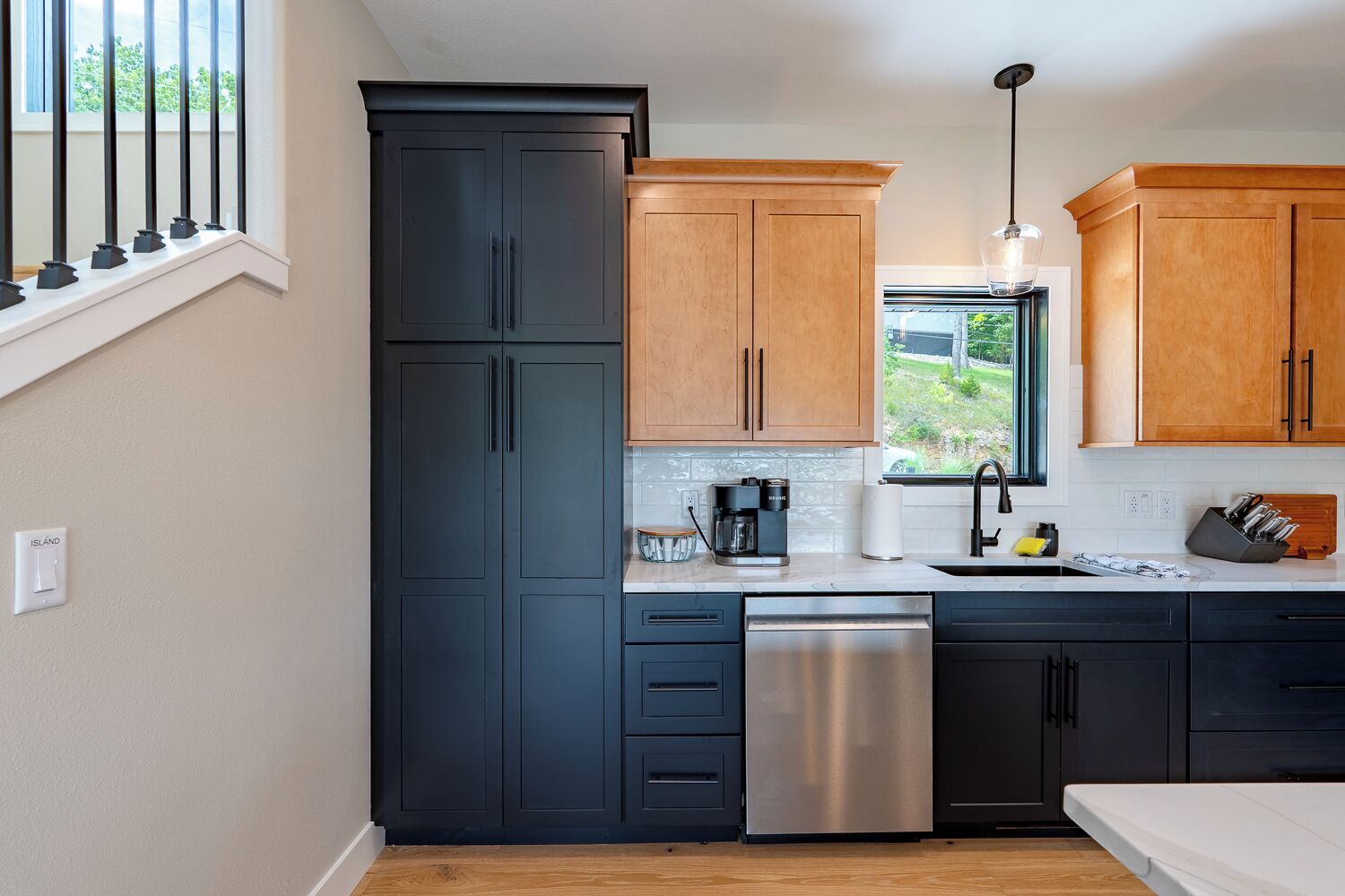 Una cocina moderna con armarios negros y de madera, un lavavajillas de acero inoxidable y una ventana con vistas a zonas verdes.