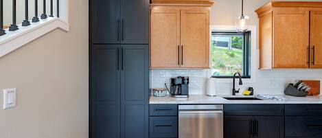 Una cocina moderna con armarios negros y de madera, un lavavajillas de acero inoxidable y una ventana con vistas a zonas verdes.