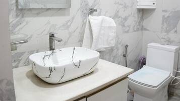 Un baño con lavamanos de mármol, inodoro, toallero y cabezal de ducha.