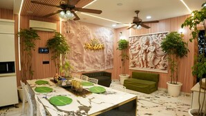 A modern living room with a marble coffee table, green sofa, ceiling fans, and decorative wall art.