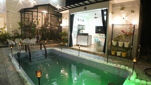 A swimming pool with a glass enclosure, outdoor seating, and potted plants.