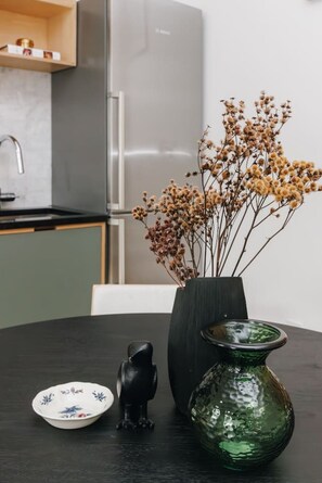 A dining table with a vase of dried flowers, a ceramic frog, and a green glass vase. - European Style Luxe 1BD, Walk to All OTR (Cincinnati)