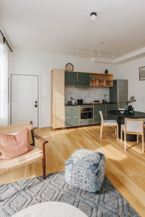 A modern kitchen with green cabinets, a dining table, and a sofa in a living area. - European Style Luxe 1BD, Walk to All OTR (Cincinnati)
