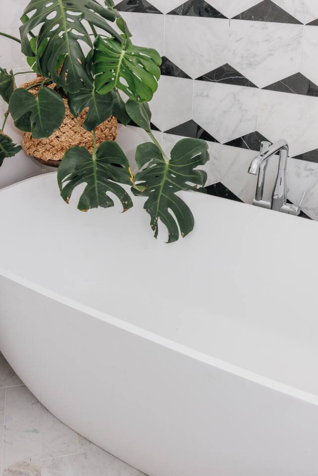 A modern bathroom with a freestanding bathtub, a sink, and a potted monstera plant.