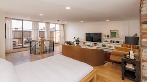 Et rummeligt soveværelse med en stor seng, en balkon med gelænder af træ, et siddeområde med sofa og lænestole, et fjernsyn og en pejs.