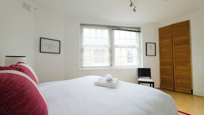 A bedroom with a large bed, a window with blinds, a wooden wardrobe, and a ceiling light fixture. - Stylish Flat Near Whitechapel - Pass the Keys (London)