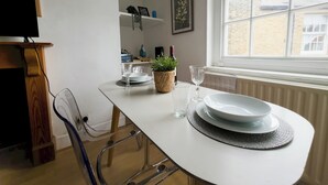 A dining area with a white table, clear glassware, a potted plant, and a window with a view of buildings. - Stylish Flat Near Whitechapel - Pass the Keys (London)