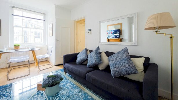A modern living room with a dark sofa, patterned cushions, a glass coffee table, a floor lamp, and a TV on a stand. - Stylish Flat Near Whitechapel - Pass the Keys (London)
