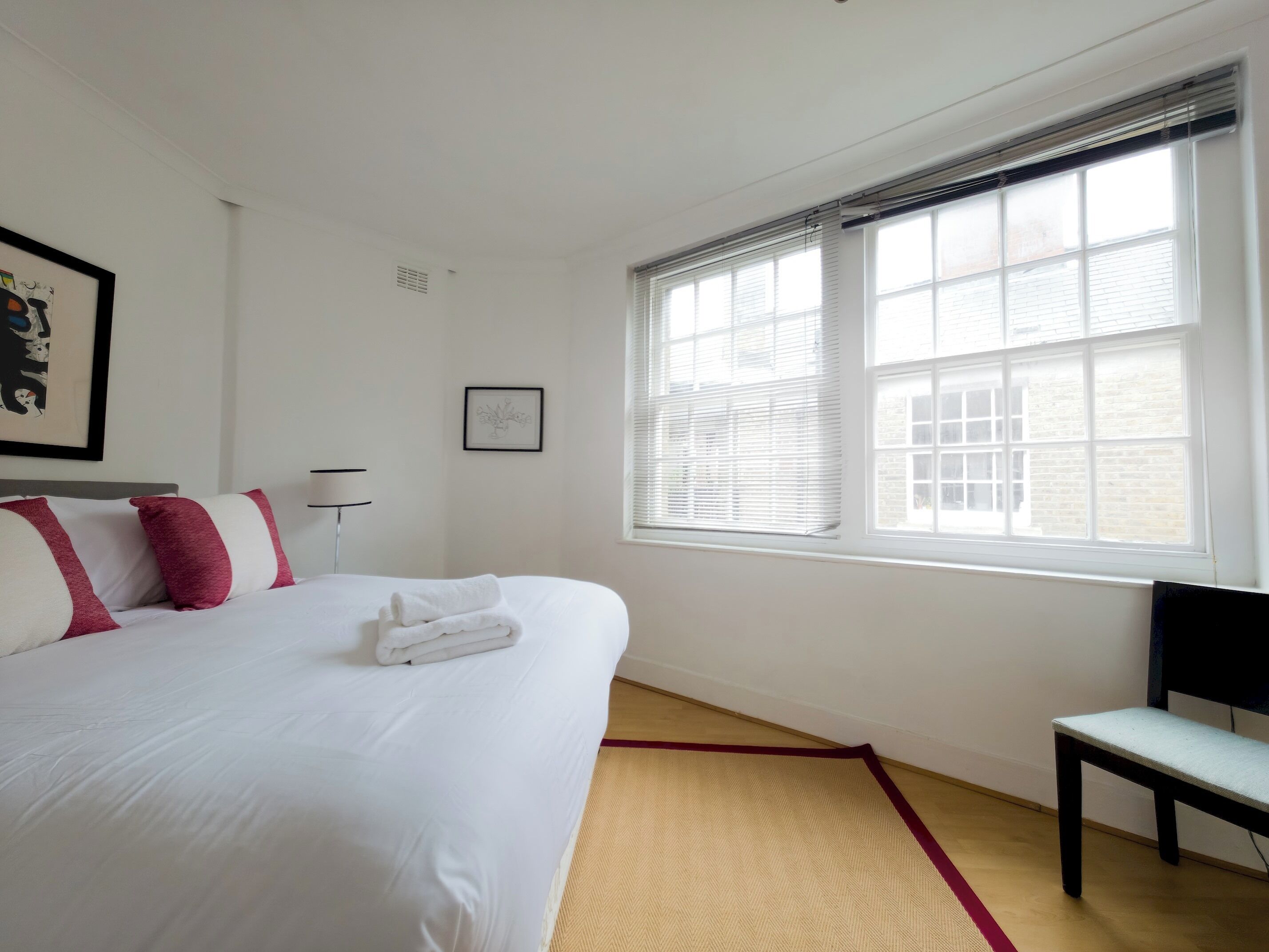 A hotel room with a large bed, a window with blinds, a chair, and a small table.