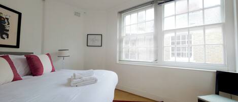A hotel room with a large bed, a window with blinds, a chair, and a small table.