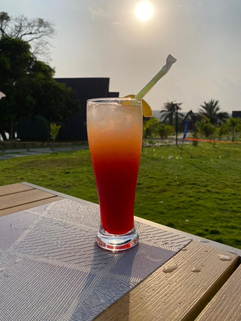 A tall glass of red beverage with a straw on a wooden table outdoors.