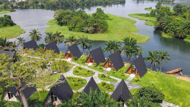A series of conical-roofed cottages with a central pathway, surrounded by lush greenery and a body of water. - Palm Island Resort (Akosombo)