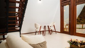 A modern living room with a sofa, two chairs, a small table with a floral arrangement, a wooden staircase, and a sliding glass door leading to an outdoor area. - Palm Island Resort (Akosombo)