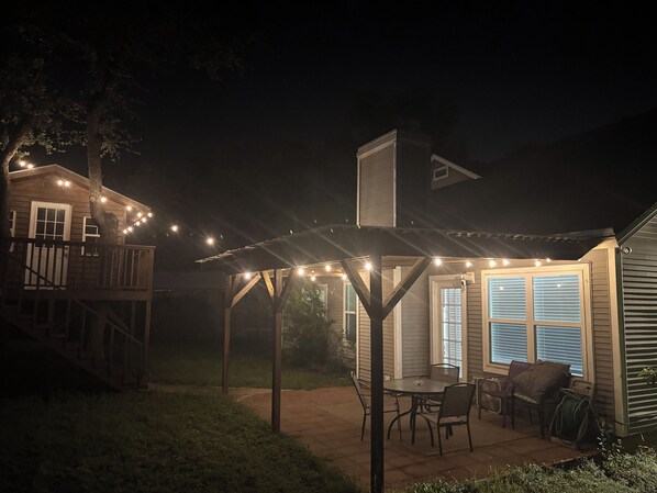 Ein überdachter Patio-Bereich mit Lichterkette, einer Holzterrasse und einem Esstisch mit Stühlen.