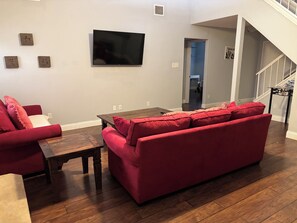 Ein Wohnzimmer mit einem roten Sofa, einem Holztisch und einem flachbildfernseher an der Wand.