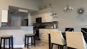 Cozinha com armários brancos, micro-ondas, fogão e área de refeições com cadeiras e mesa.