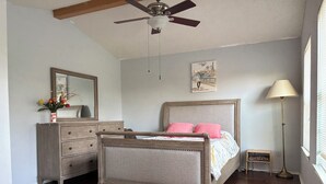 Quarto com cama, penteadeira, espelho, ventilador de teto, obra de arte, luminária e tapete com padrão de zebra.